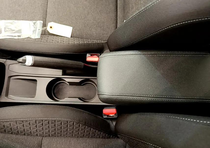 Vue rapprochée de la console centrale noire avec frein à main et porte-gobelets entre les sièges avant en tissu gris foncé.