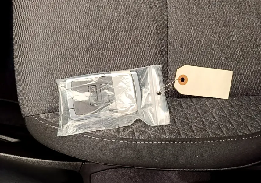 Gros plan sur une clé de voiture Renault Clio Business TCe 100 2020 dans un sachet plastique, posée sur un siège tissu gris.