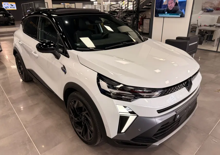 Renault Captur E-Tech blanc nacré toit noir, vue 3/4 avant droit en intérieur avec jantes noires et feux LED distinctifs.