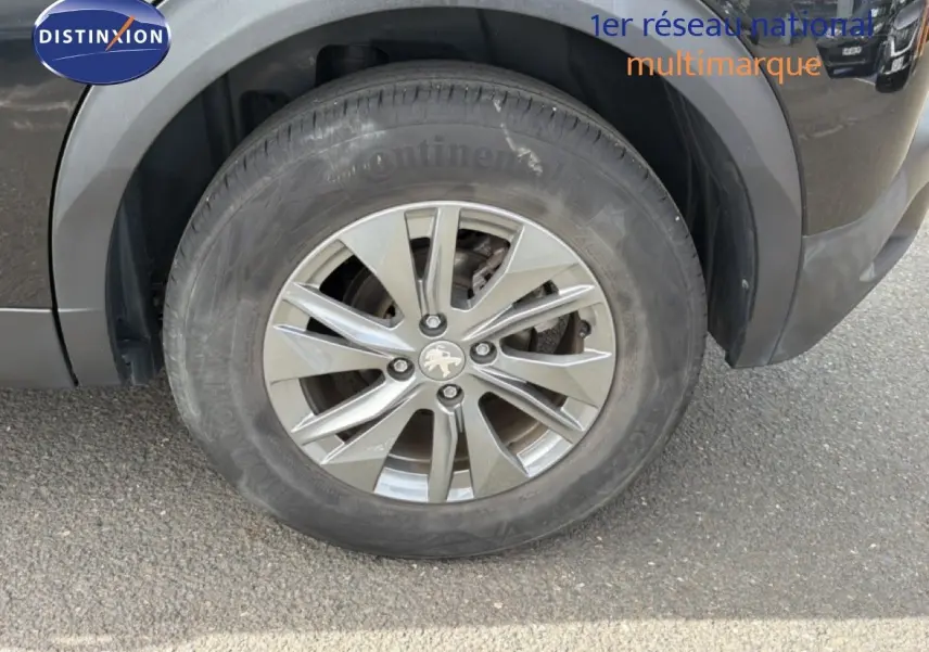 Gros plan sur la roue avant gauche d'un Peugeot 2008 noir perle métal, avec jante alliage 16 pouces et logo lion au centre.