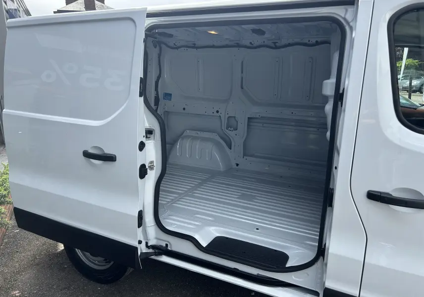 Vue latérale gauche du Renault Trafic Fourgon blanc glacier avec porte coulissante ouverte montrant l’espace de chargement vide.