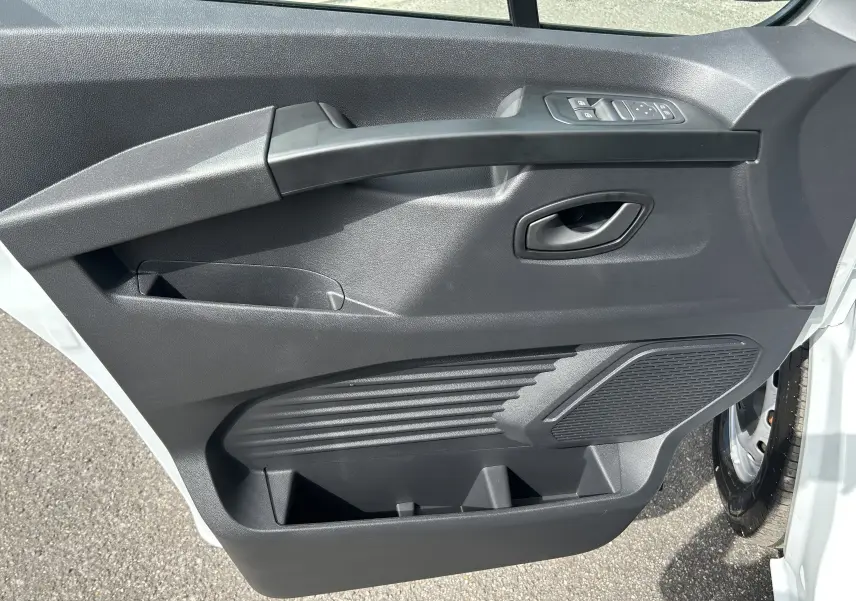Vue rapprochée de la porte avant droite du Renault Trafic Fourgon blanc glacier, avec commandes de vitres et haut-parleur intégré.