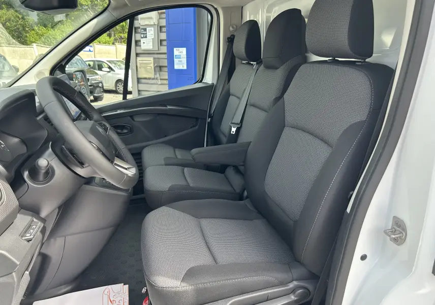 Vue intérieure côté conducteur du Renault Trafic Fourgon blanc glacier 2025, montrant les sièges tissu et le volant multifonction.