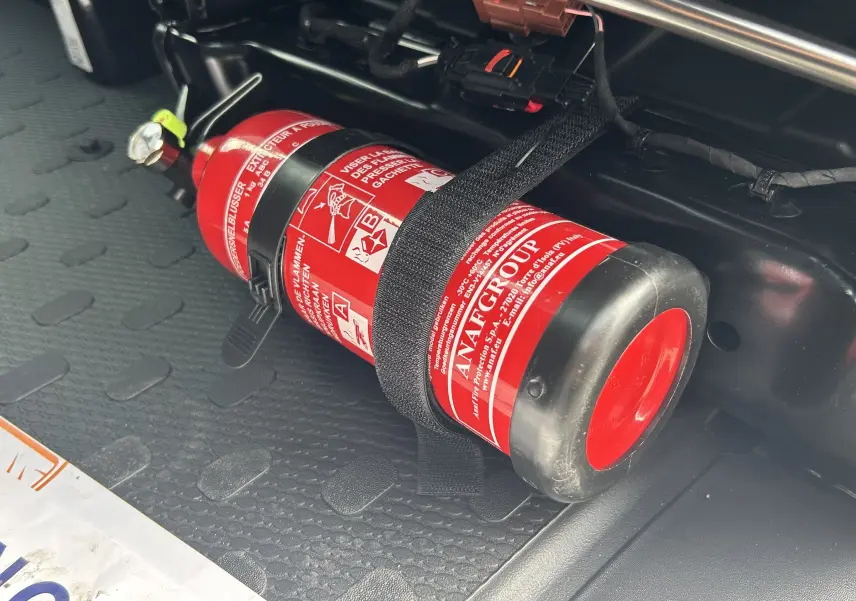 Gros plan sur l’extincteur rouge fixé au plancher noir du Renault Trafic Fourgon blanc Glacier.