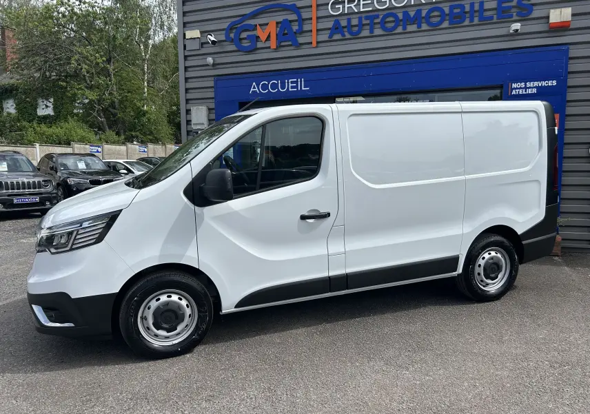 Vue de profil côté gauche d'un Renault Trafic Fourgon blanc Glacier stationné devant un garage automobile.