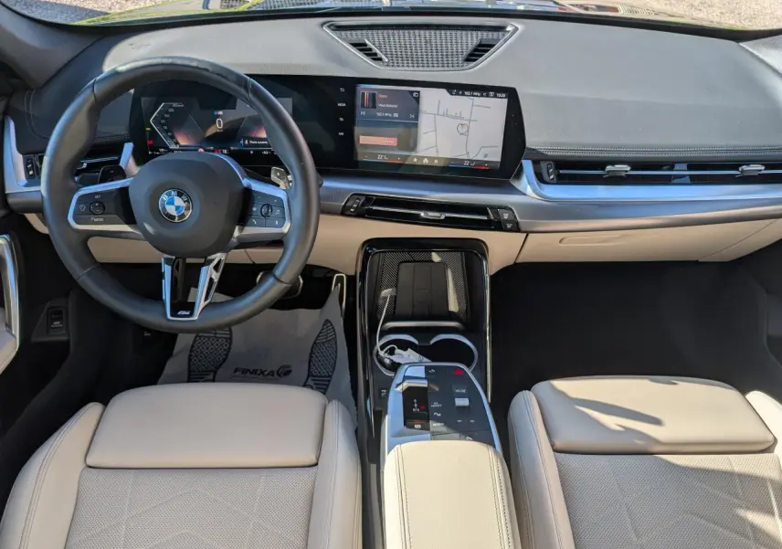 Vue intérieure frontale du BMW X1 2024 M Sport avec sellerie similicuir Oyster claire et écran tactile incurvé.