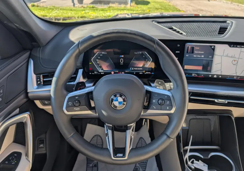 Vue intérieure centrée sur le volant M cuir noir et le tableau de bord numérique du BMW X1 noir 2024.