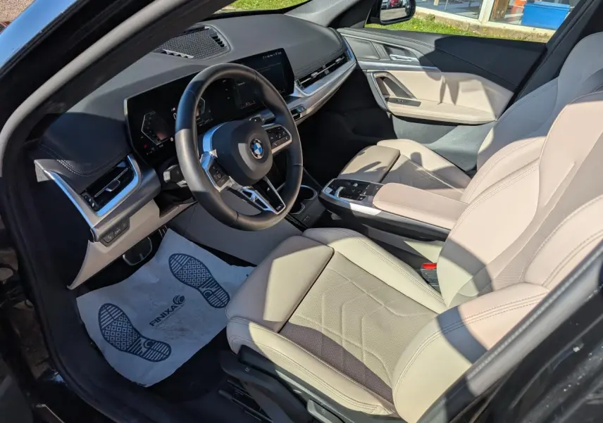 Vue intérieure côté conducteur du BMW X1 noir 2024, sellerie similicuir Oyster claire et tableau de bord moderne.