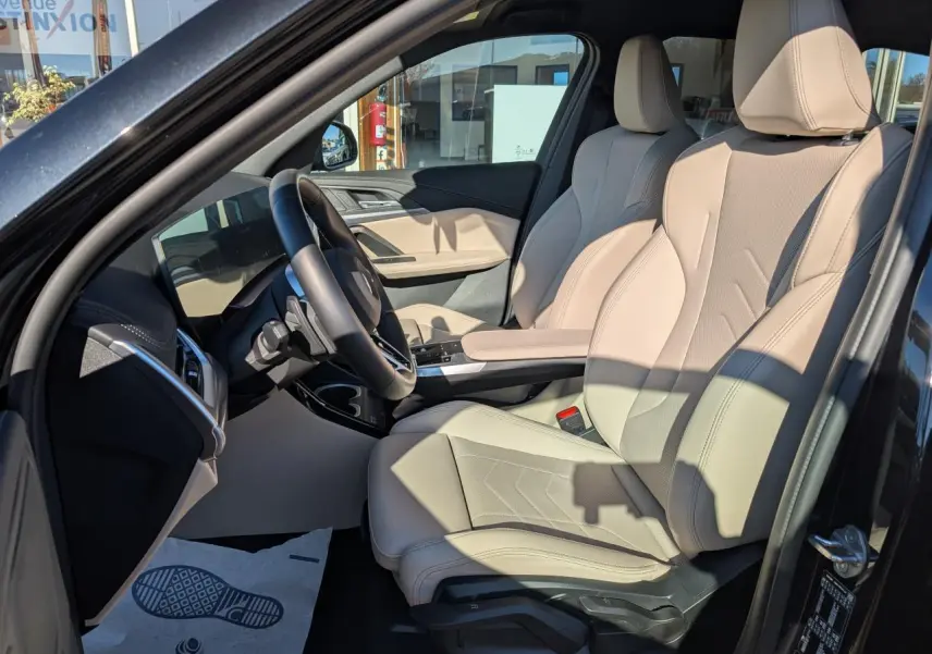 Intérieur côté conducteur BMW X1 noir 2024, sièges sport similicuir Oyster beige et volant M cuir.