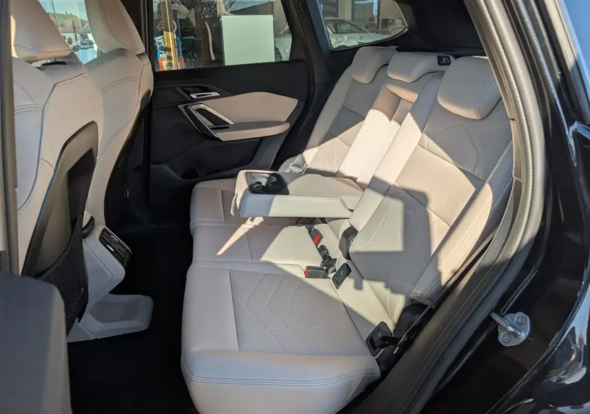 Vue intérieure côté droit sur la banquette arrière en similicuir Oyster du BMW X1 noir avec accoudoir central déployé.