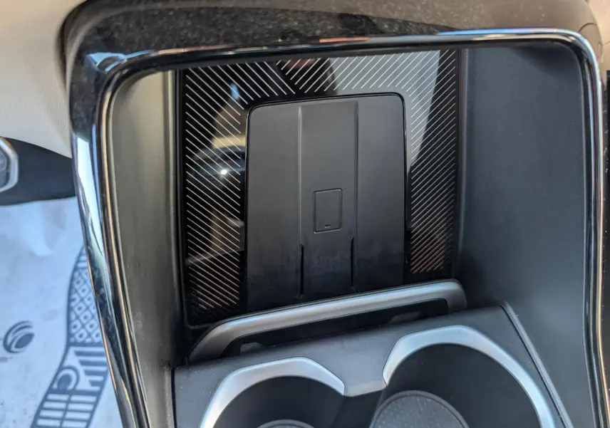 Détail de la console centrale noire du BMW X1 2024 avec zone de recharge sans fil et porte-gobelets intégrés.