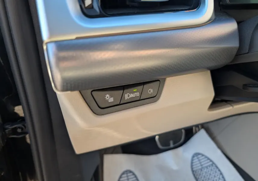 Détail intérieur côté gauche avec commandes d'éclairage sur tableau de bord beige et noir du BMW X1 noir 2024 M Sport.