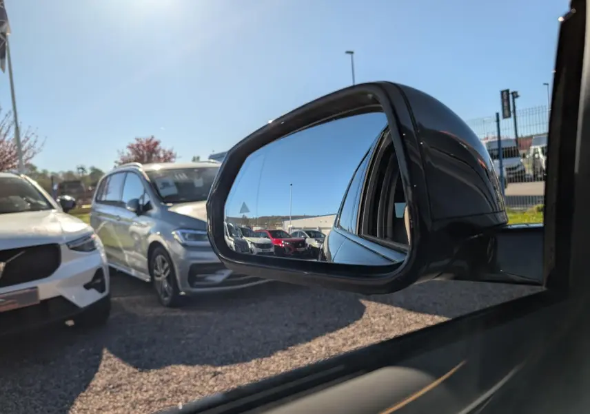 Rétroviseur extérieur droit noir du BMW X1 2024, reflétant plusieurs voitures sur un parking en plein jour.