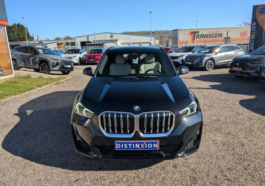 Vue frontale d’un BMW X1 noir métallisé avec calandre chromée et phares LED avancés, sur un parking extérieur.
