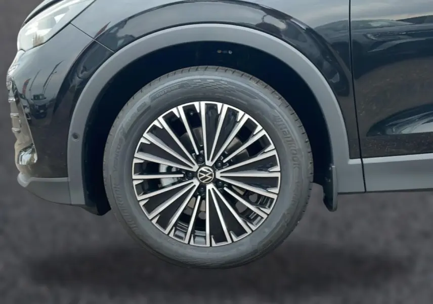 Gros plan sur la roue avant gauche du Volkswagen Tiguan noir 2025 avec jante alliage multibranches.