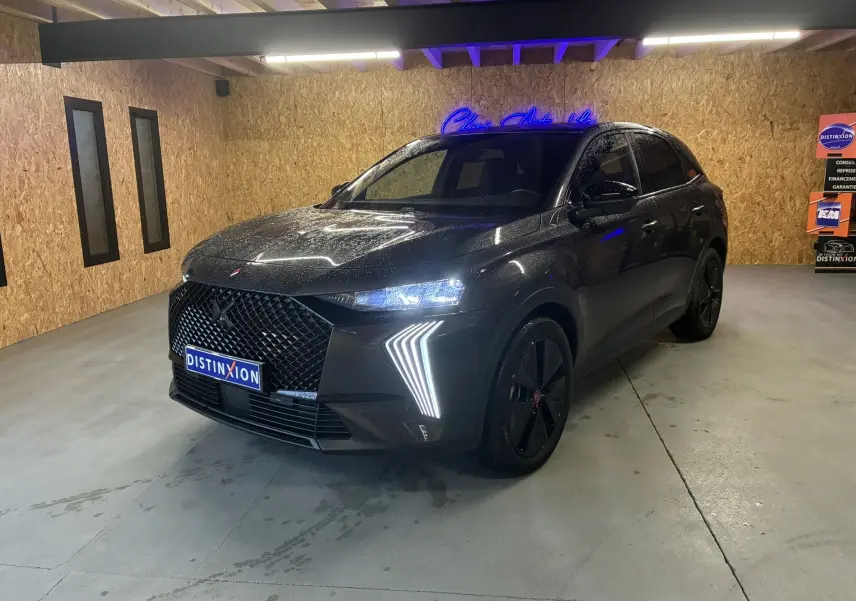 DS7 E-TENSE gris en 3/4 avant droit, avec calandre distinctive et feux LED en forme de flèche allumés.