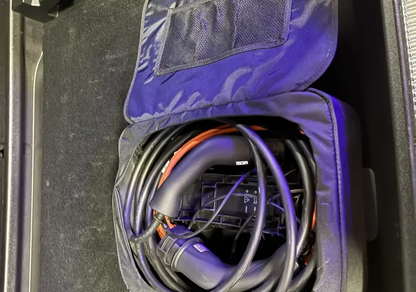Câble de recharge hybride enroulé dans un sac noir, rangé dans le coffre d'un DS7 gris 2024.