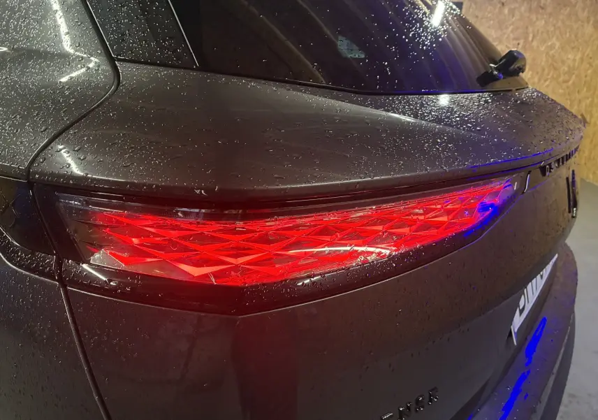 Gros plan sur le feu arrière droit rouge du DS7 E-TENSE gris 2024, avec gouttes d'eau sur la carrosserie brillante.