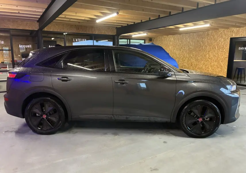 Vue de profil côté gauche du DS7 E-TENSE gris 2024, avec jantes noires et toit légèrement incliné dans un garage.