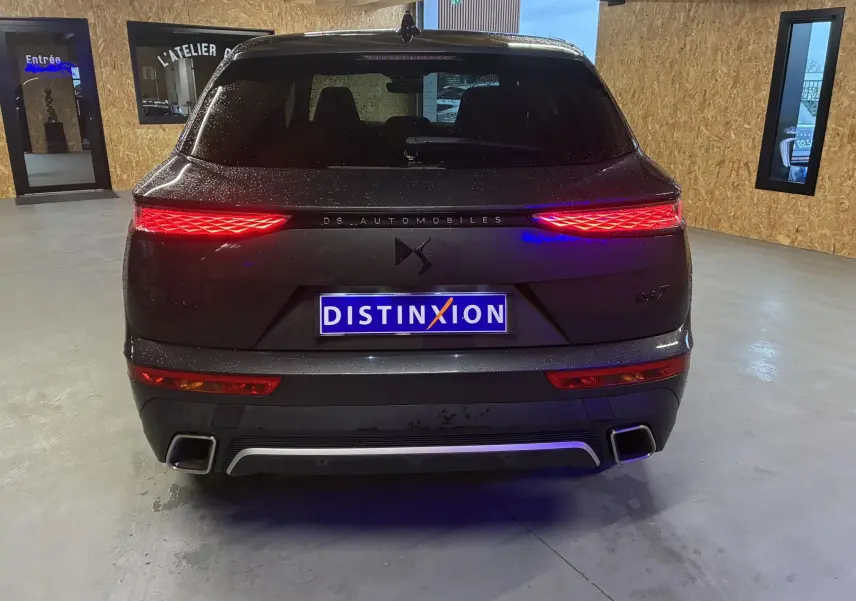 Vue arrière d'un DS7 gris 2024 avec feux arrière allumés et double sortie d'échappement rectangulaire.