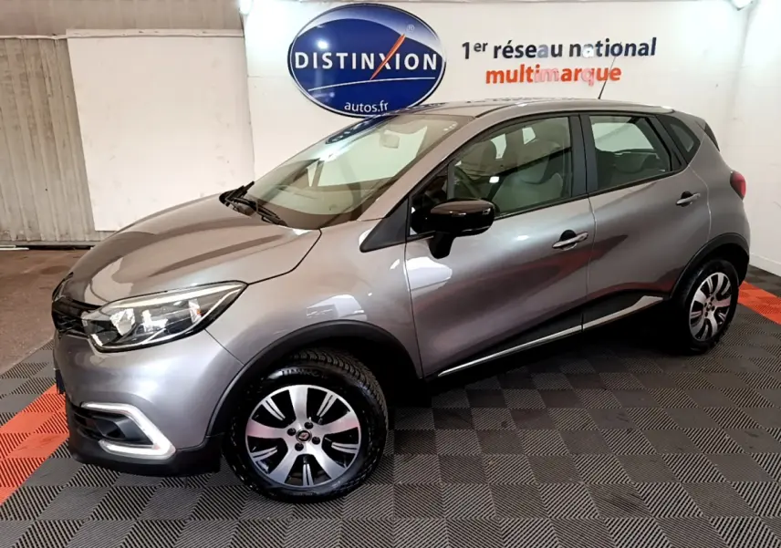Renault Captur Business gris foncé vu en 3/4 avant droit dans un showroom avec logo Distinxion en arrière-plan.