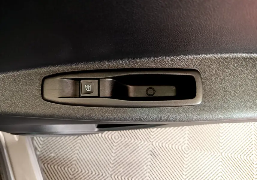 Gros plan sur le bouton de commande de la vitre électrique dans la portière intérieure d’un Renault Captur gris foncé.