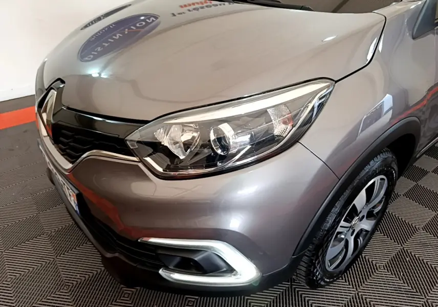 Vue 3/4 avant droit d'un Renault Captur Business gris foncé, mettant en valeur ses phares ellipsoïdaux et sa calandre chromée.
