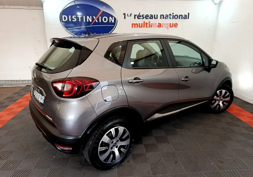 Vue 3/4 arrière droite d’un Renault Captur gris foncé 2018 dans un showroom avec logo Distinxion en arrière-plan.