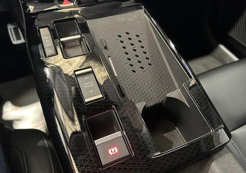 Vue rapprochée de la console centrale noire brillante du Citroën C5 Aircross II Hybrid 2026 avec commandes électroniques et porte-gobelet.