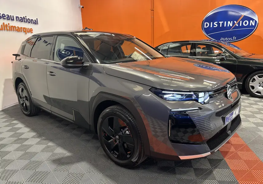 Vue 3/4 avant droite du Citroën C5 Aircross II Max Hybrid gris Platinium avec toit noir dans un showroom.