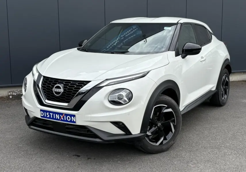 Nissan Juke blanc perle en 3/4 avant droit, avec jantes alliage noires et calandre chromée distinctive.