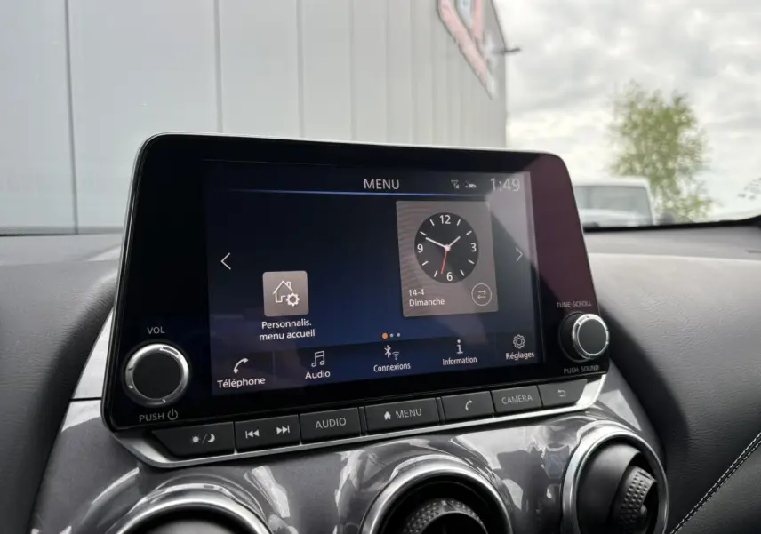 Écran tactile central du Nissan Juke 2024 affichant le menu principal avec commandes audio et caméra, intérieur noir.
