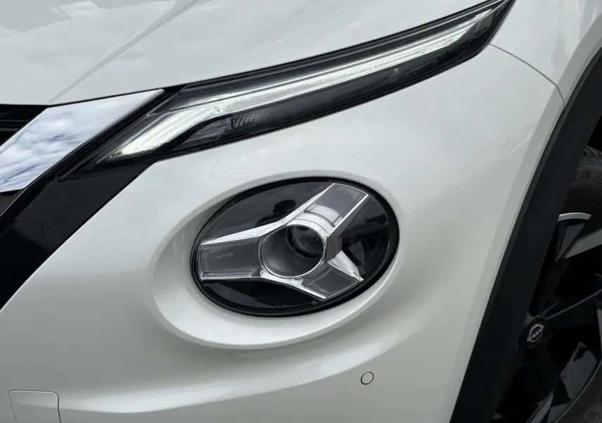 Gros plan sur le phare antibrouillard avant droit du Nissan Juke blanc perle 2024 avec détails chromés et calandre noire.