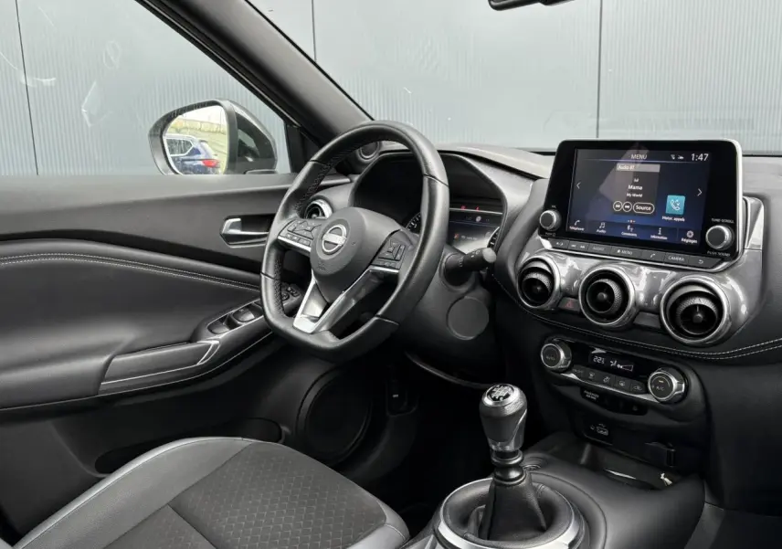 Intérieur côté conducteur du Nissan Juke 2024, tableau de bord noir avec écran tactile et boîte manuelle visible.