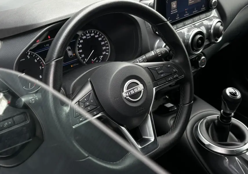 Vue rapprochée de l'intérieur du Nissan Juke blanc perle 2024, volant multifonction et levier de vitesse manuel visibles.