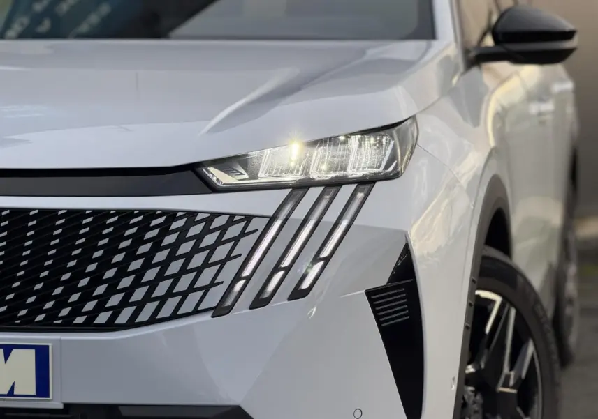 Gros plan sur l'avant droit du Peugeot 3008 blanc Okénite, mettant en valeur les phares LED et la calandre distinctive.