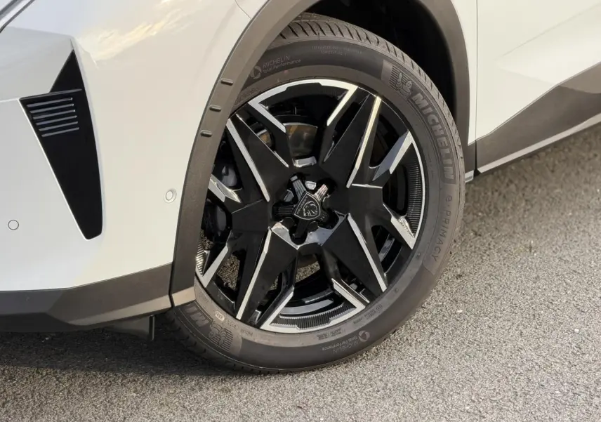 Gros plan sur la roue avant droite du Peugeot 3008 Hybrid blanc Okénite avec jante alliage noire et argentée.