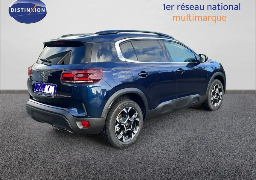 Vue 3/4 arrière droite d’un Citroën C5 Aircross 2025 bleu eclipse métal avec jantes alliage et barres de toit.