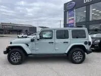 Vue de profil droit d'un Jeep Wrangler Unlimited vert métal 2023 hybride rechargeable devant un concessionnaire.