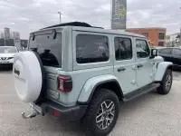 Vue 3/4 arrière droite d'un Jeep Wrangler Unlimited 2023 vert métal avec roue de secours et toit rigide noir.