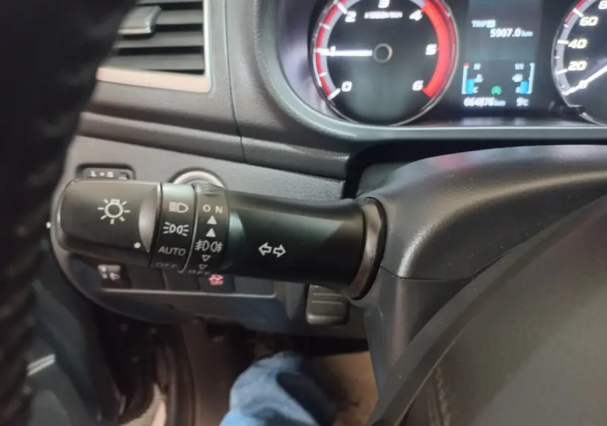 Gros plan sur la manette de commande des phares et clignotants du Mitsubishi L200 gris foncé, tableau de bord en arrière-plan.