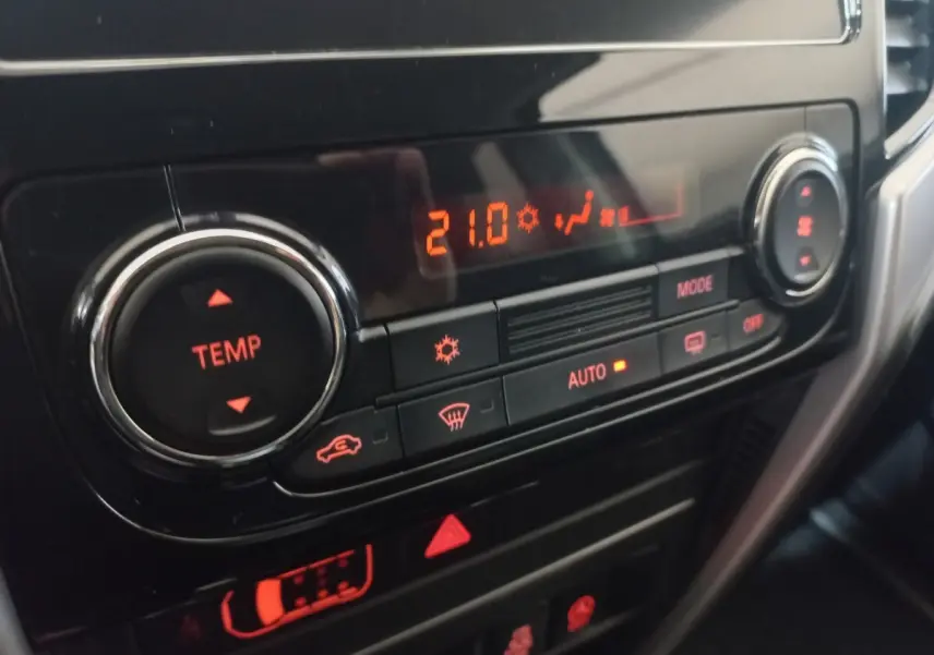 Gros plan sur la commande de climatisation digitale du Mitsubishi L200 gris foncé, affichant 21°C en mode automatique.