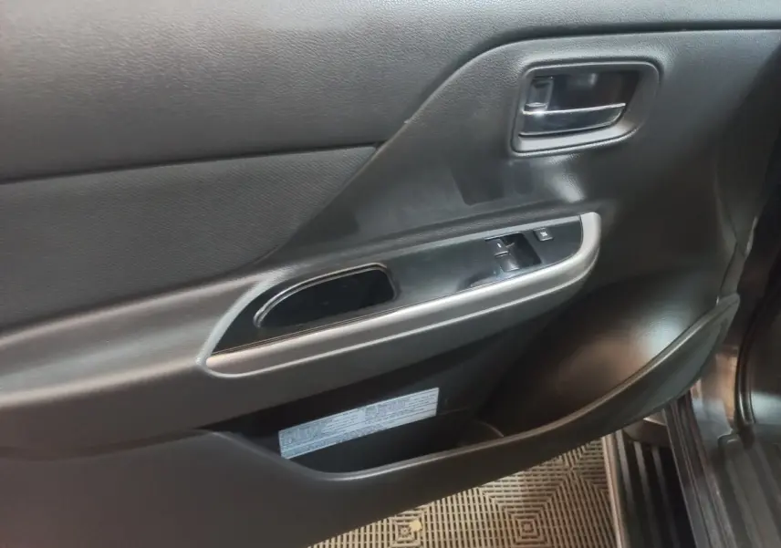 Vue rapprochée de la porte intérieure côté conducteur du Mitsubishi L200 gris foncé, avec commandes de vitres et poignée chrome.