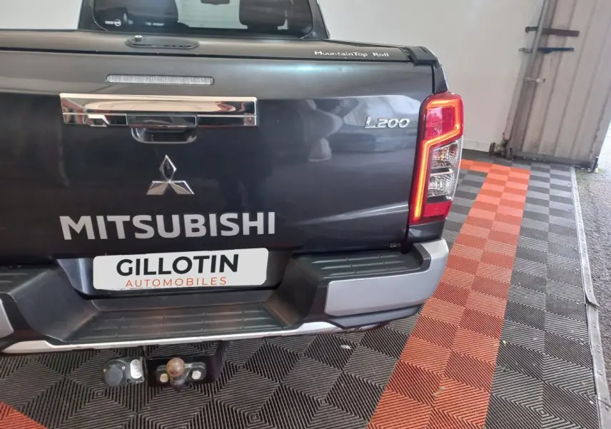 Vue arrière du pick-up Mitsubishi L200 gris foncé avec hayon fermé et feux arrière allumés en intérieur.