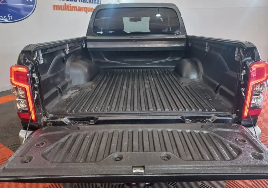 Vue arrière du pick-up Mitsubishi L200 gris foncé avec benne ouverte et ridelles visibles dans un showroom.