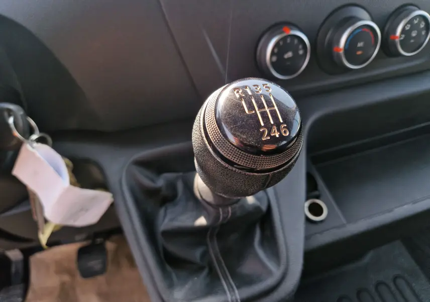 Gros plan sur le levier de vitesses manuel noir du Renault Master Châssis Double Cabine blanc, avec commandes de climatisation en arrière-plan.