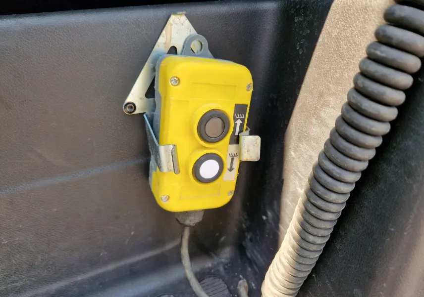 Gros plan sur un boîtier de commande jaune fixé à l'intérieur d'un Renault Master blanc, avec deux boutons noirs et blanc.