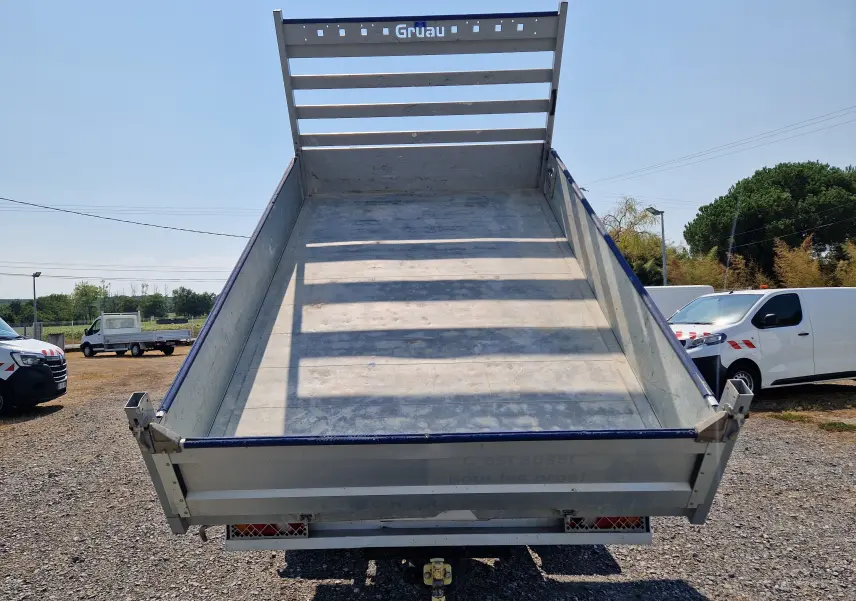 Vue arrière en contre-plongée d’une benne aluminium relevée sur un Renault Master blanc, avec coffre et ridelle marquée Gruau.
