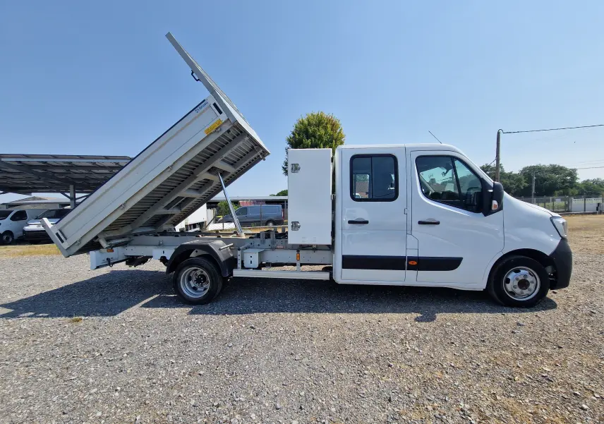 Vue latérale droite d'un Renault Master blanc avec benne relevée et coffre latéral blanc sur châssis double cabine.