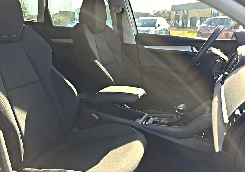Vue intérieure côté droit du Skoda Karoq 2025, sièges noirs avec accoudoir central et volant multifonction.